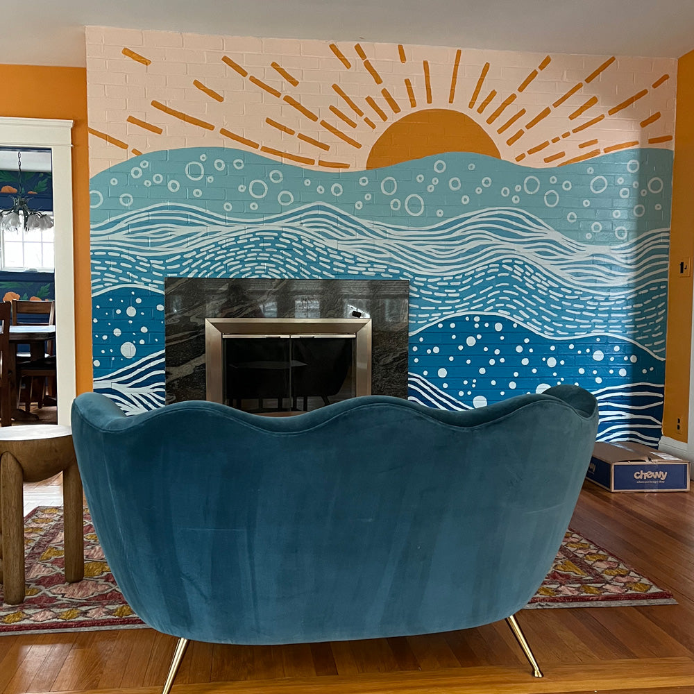 living room with a blue couch and sunset ocean mural on a brick wall