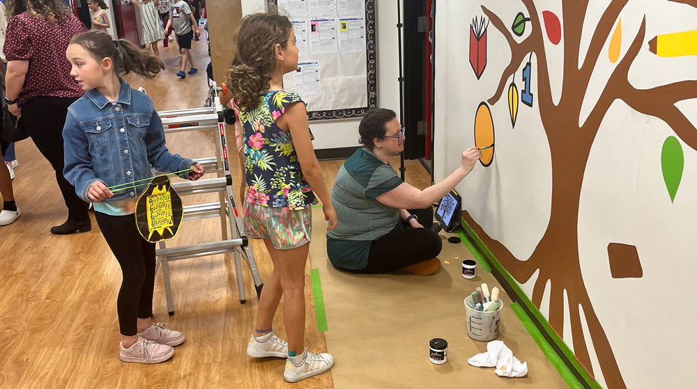 Hannah Pearlman painting a mural while children look on
