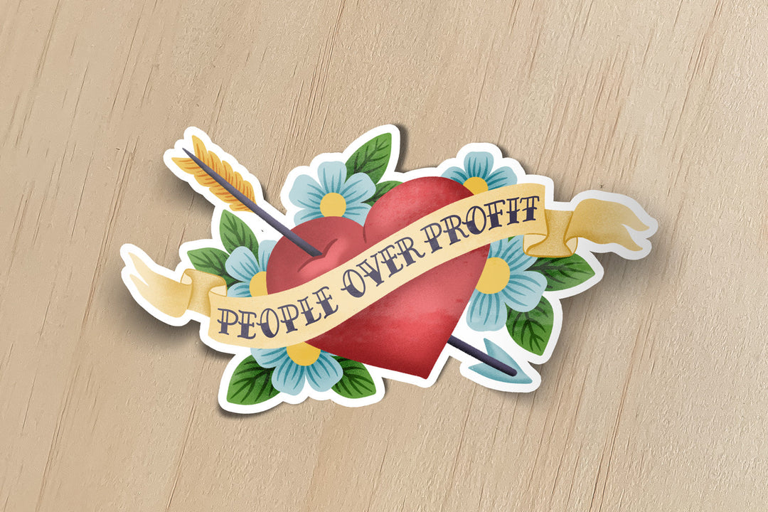 A sticker of an illustrated heart and arrow in a tattoo style that says "people over profit"