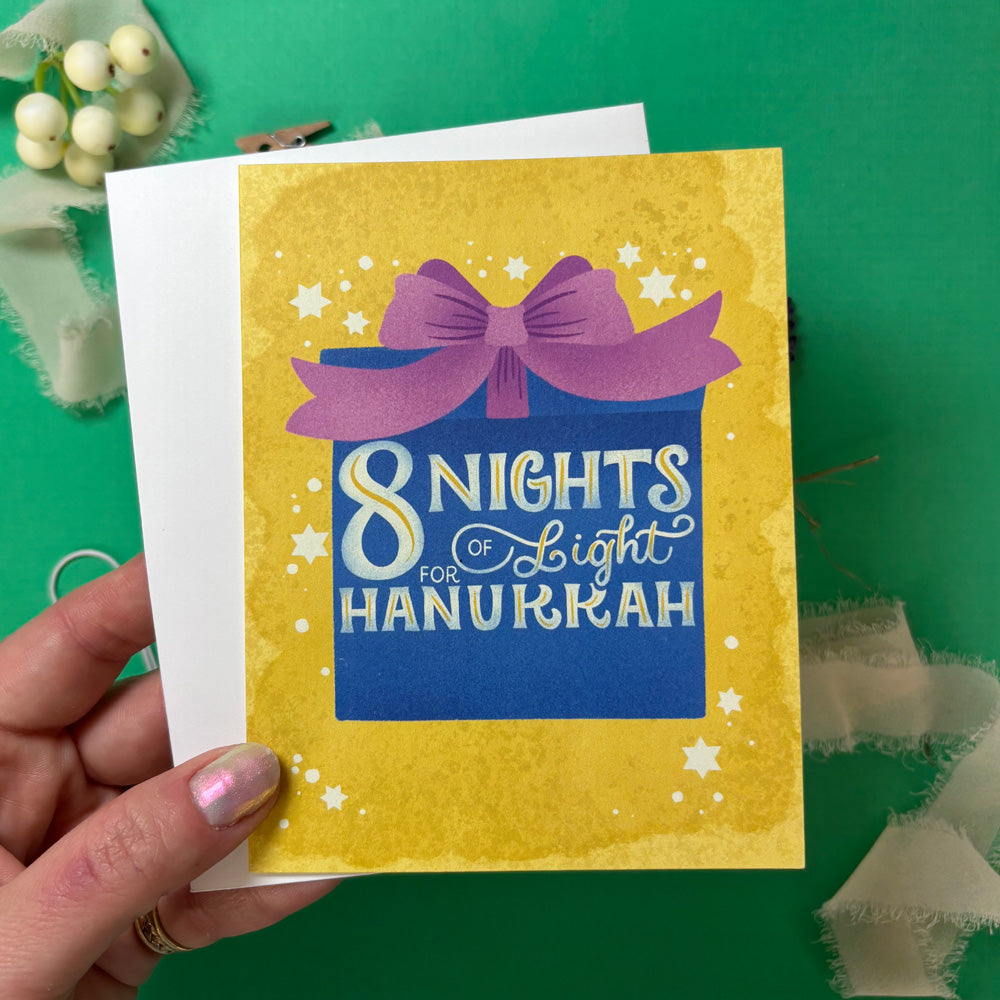 Hand holding a Hanukkah card with a purple bow and text on a green background