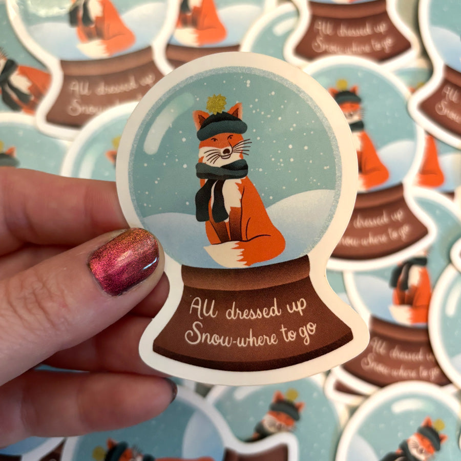 Vinyl sticker with illustration of a snow globe with a fox wearing a hat and scarf, that says "all dressed up snow where to go"