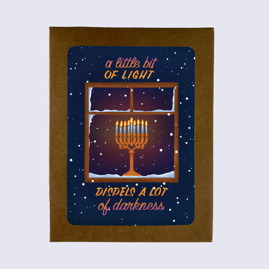 A greeting card with a Hanukkah theme, showing a window with lit candles and snowflakes, with the text 'A Little Bit of Light Dispels a Lot of Darkness'.