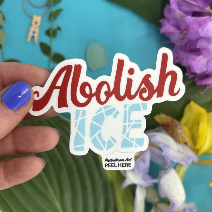 Hand holding a sticker with 'Abolish ICE' text against a floral background