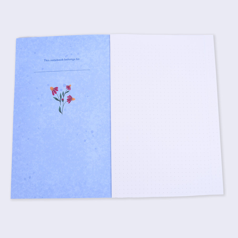 open flat lay notebook with dot grid pages and blue inside cover has a small flower illustration and text "this notebook belongs to"