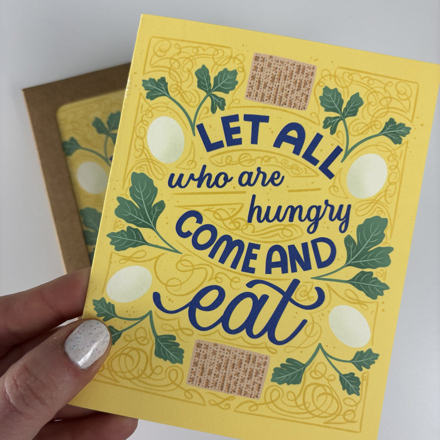 Yellow card with blue text 'Let all who are hungry come and eat' held by a hand.