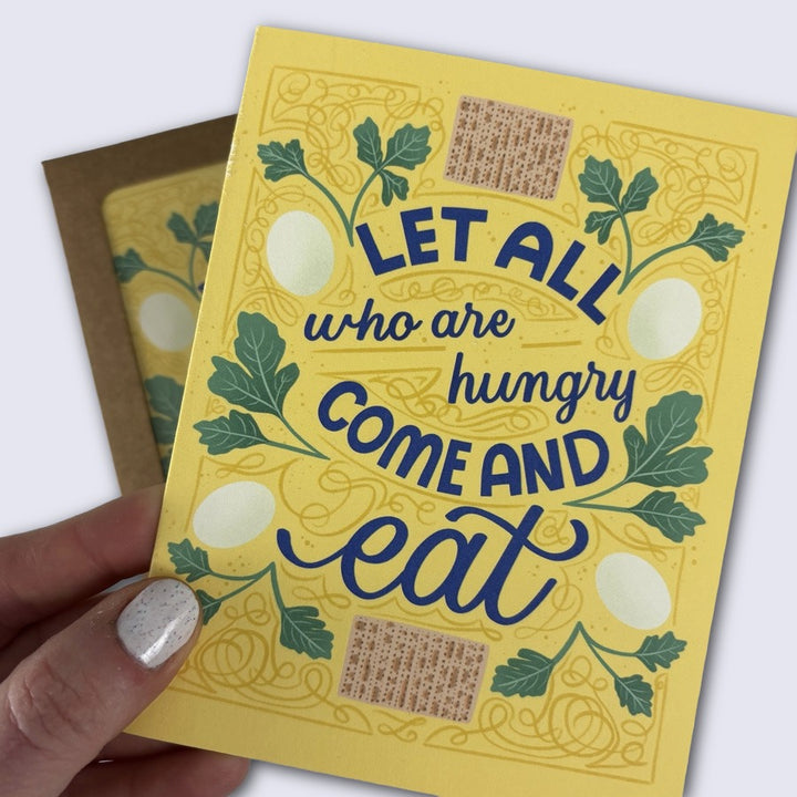 Yellow card with blue text 'Let all who are hungry come and eat' held by a hand.