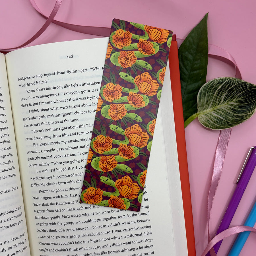 a bookmark with an illustration of a two headed snake marks the page in an open book on a pink background
