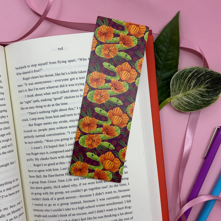 a bookmark with an illustration of a two headed snake marks the page in an open book on a pink background