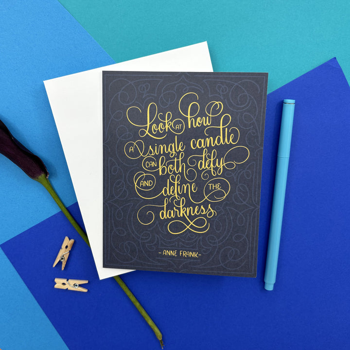 hanukkah card with Anne Frank quote "look at how a single candle can both defy and define the darkness" on a colorful background