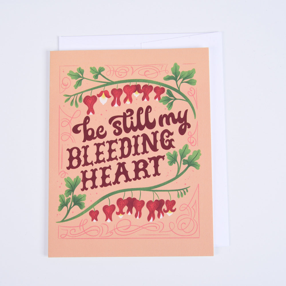 A folded greeting card with a floral design and the phrase 'Be Still My Bleeding Heart' and an illustration of bleeding heart flowers