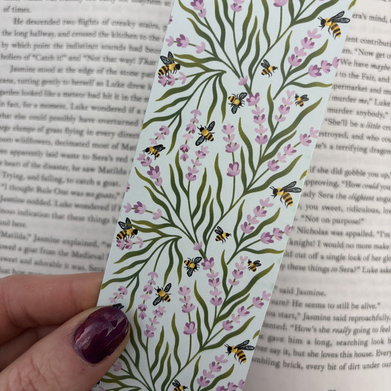 hand holding a bookmark with illustrations of bees and lavender