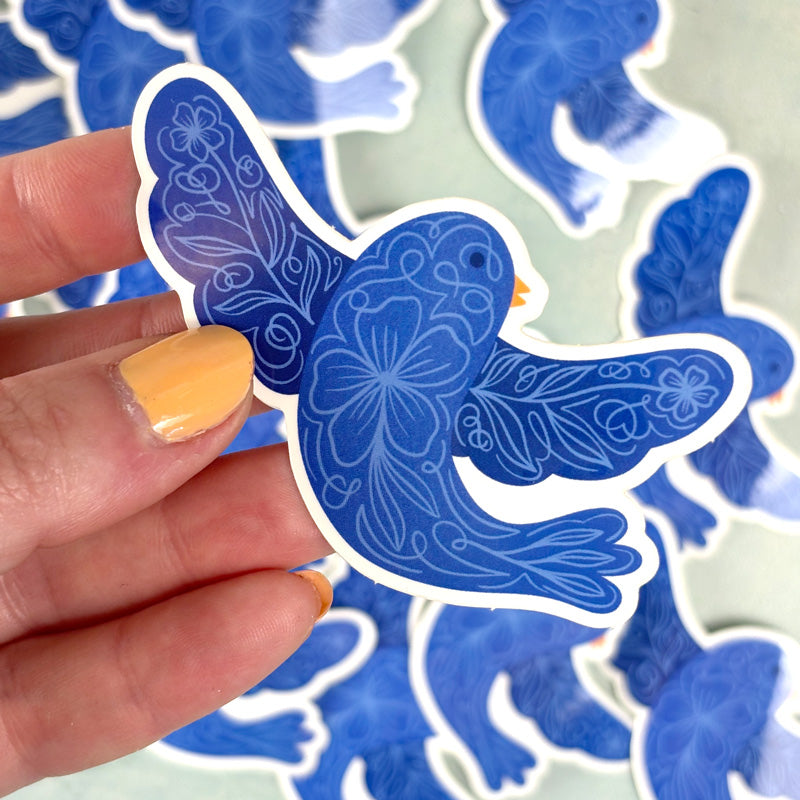 hand holding A blue sticker of a bird with floral patterns on its body and wings