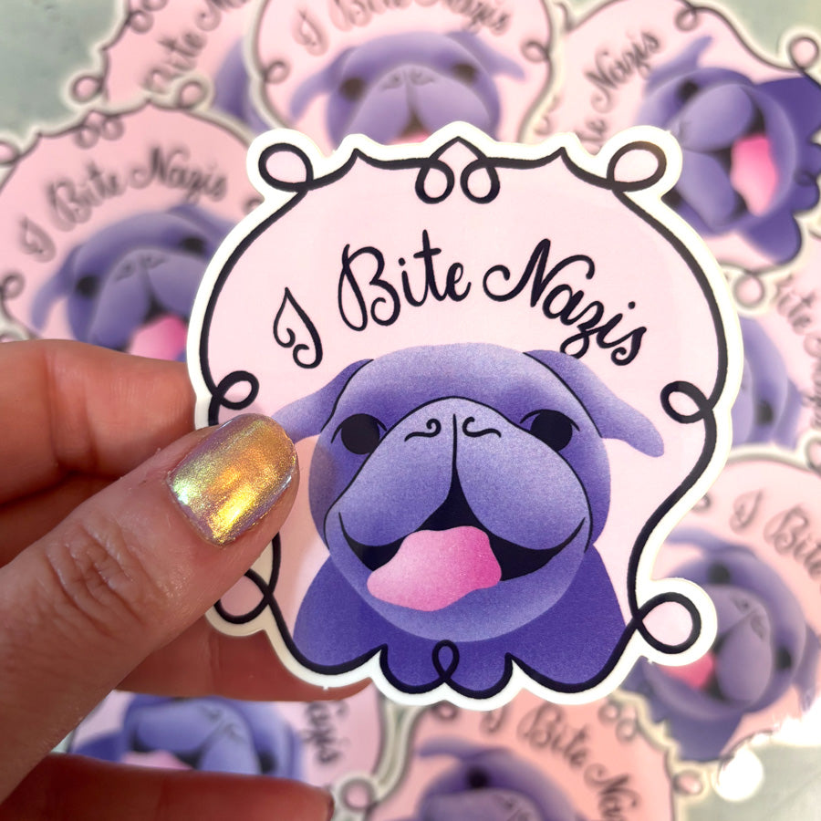 Sticker with a purple dog and 'I Bite Nazis' text held by a hand with colorful nail polish, surrounded by similar stickers.