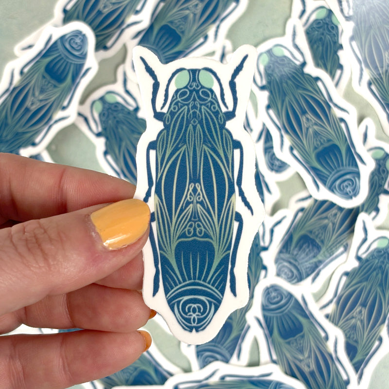 hand holding A sticker of a blue beetle with ornate floral designs