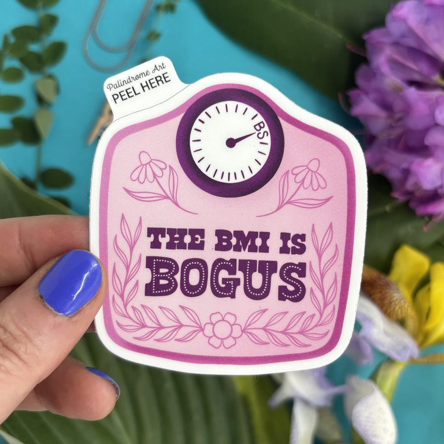 Sticker with text BMI is Bogus held by a hand against a floral background