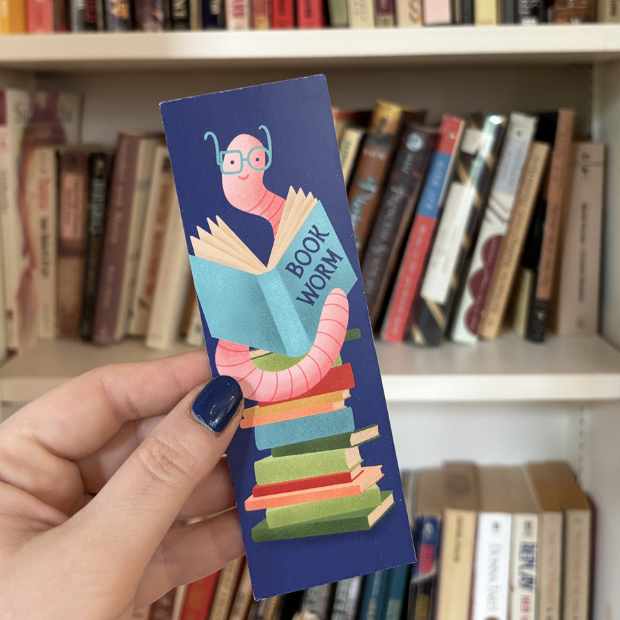 Hand holding a colorful bookmark with a 'Book Worm' design in front of a bookshelf.