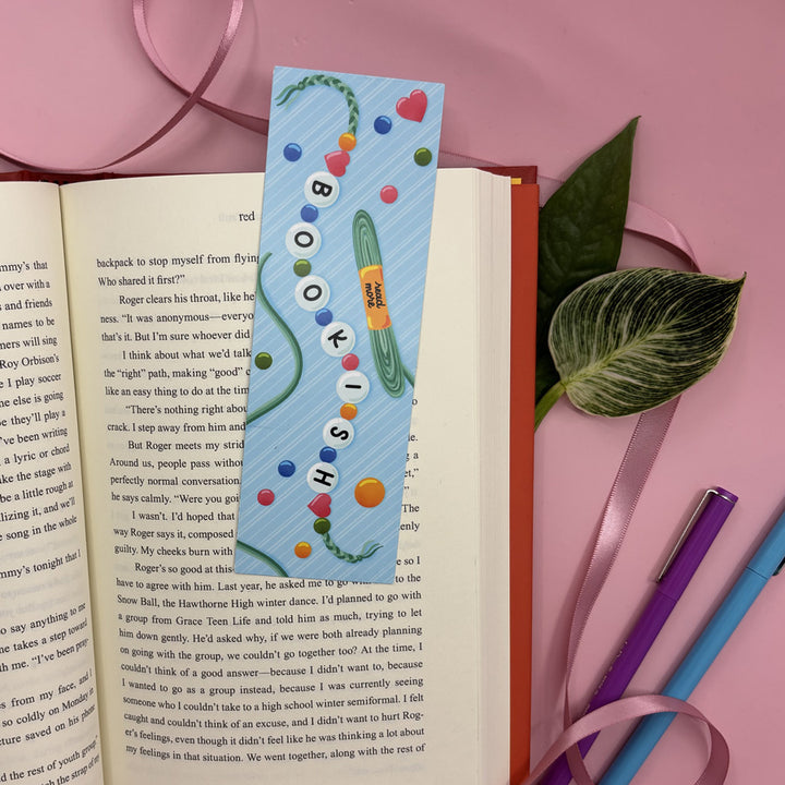 bookmark with illustration of a friendship bracelet that says "bookish" on an open book with a pink background