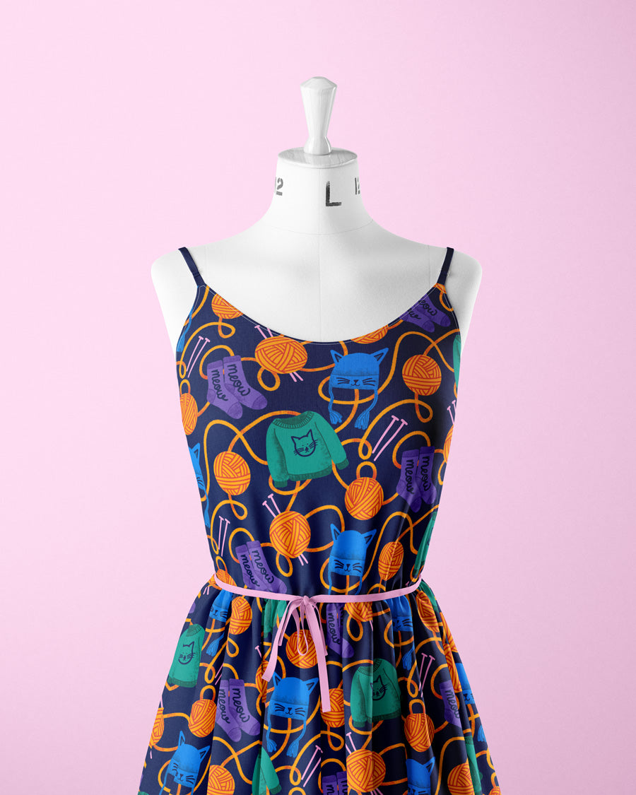 Colorful dress with yarn ball pattern on a mannequin against a pink background