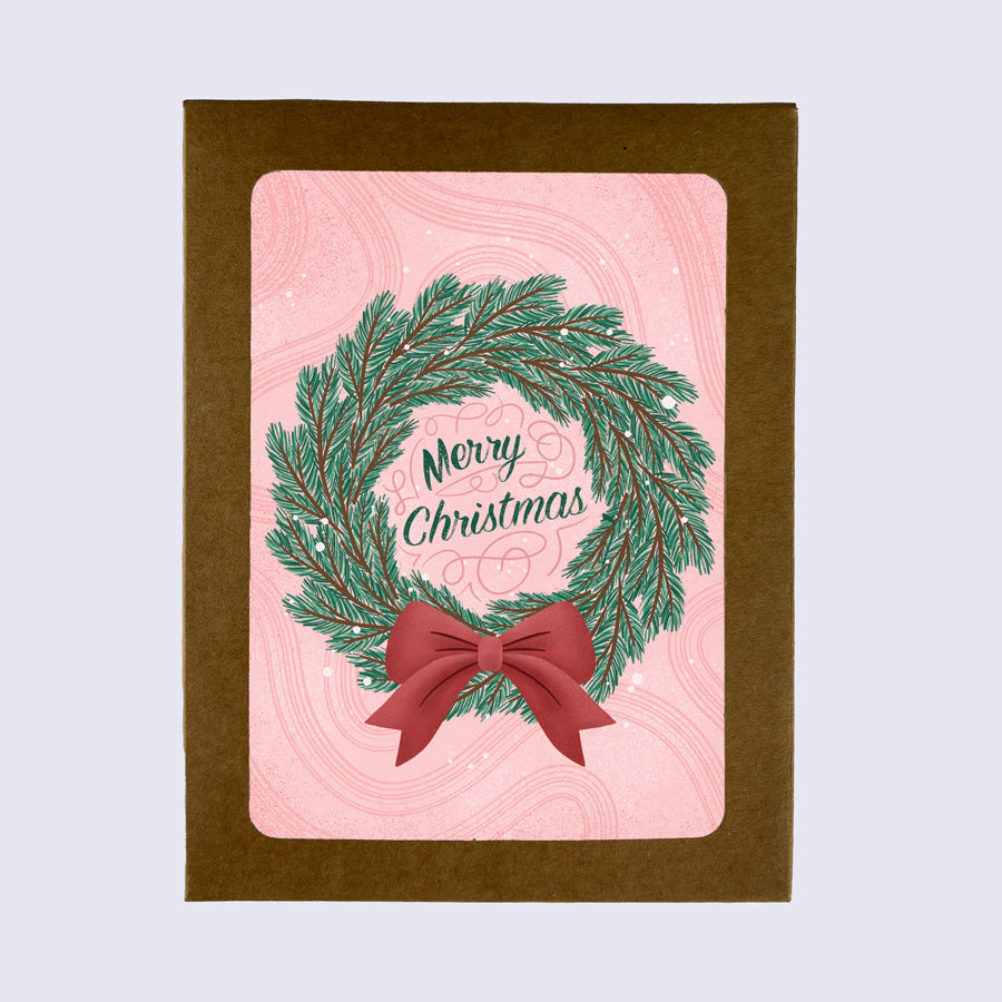 A folded greeting card with a Christmas wreath design and 'Merry Christmas' text, paired with a bright white envelope.
