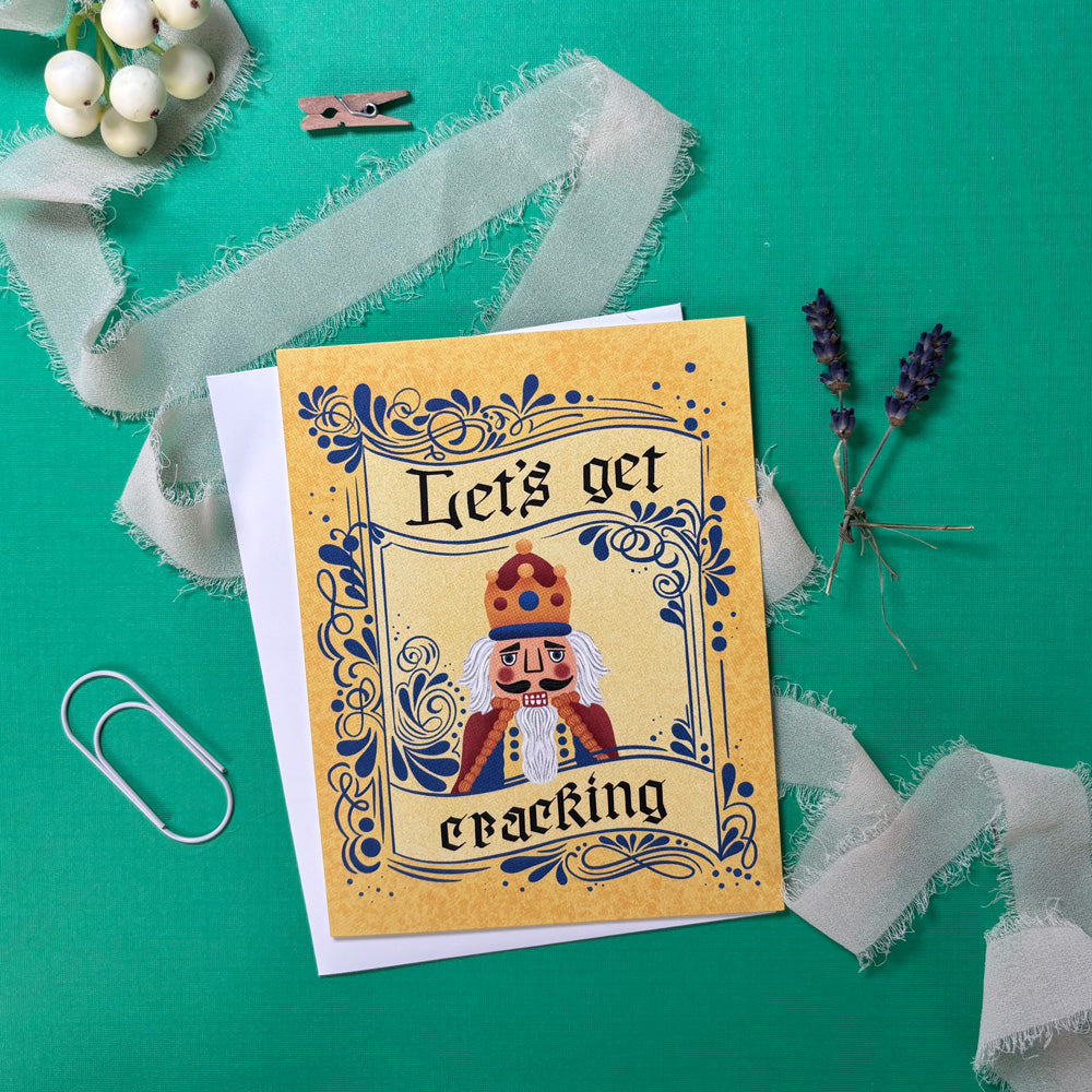 Greeting card with nutcracker design and text 'Let's get cracking' on a green background with decorative elements.