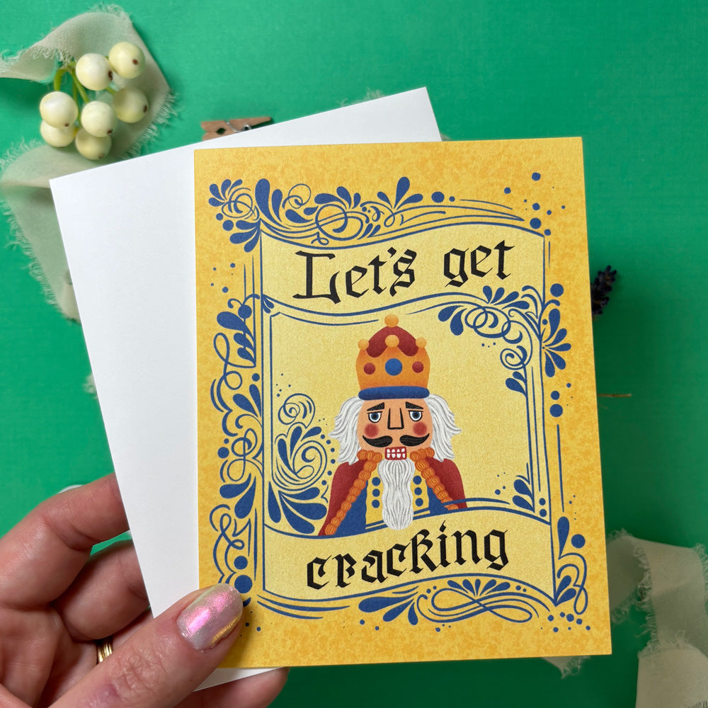 Greeting card with Nutcracker design and text 'Let's get e-packing' held by a hand on a green background.