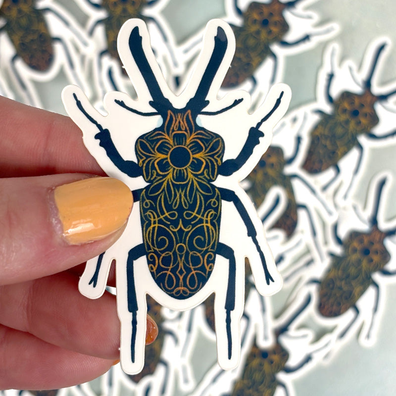 hand holding A sticker depicting a blue stag beetle with ornate red orange and blue patterns.