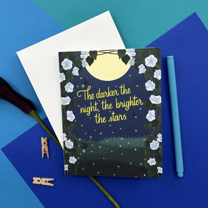 greeting card with moonlight flowers at night and text "the darker the night, the brighter the stars" on a blue background