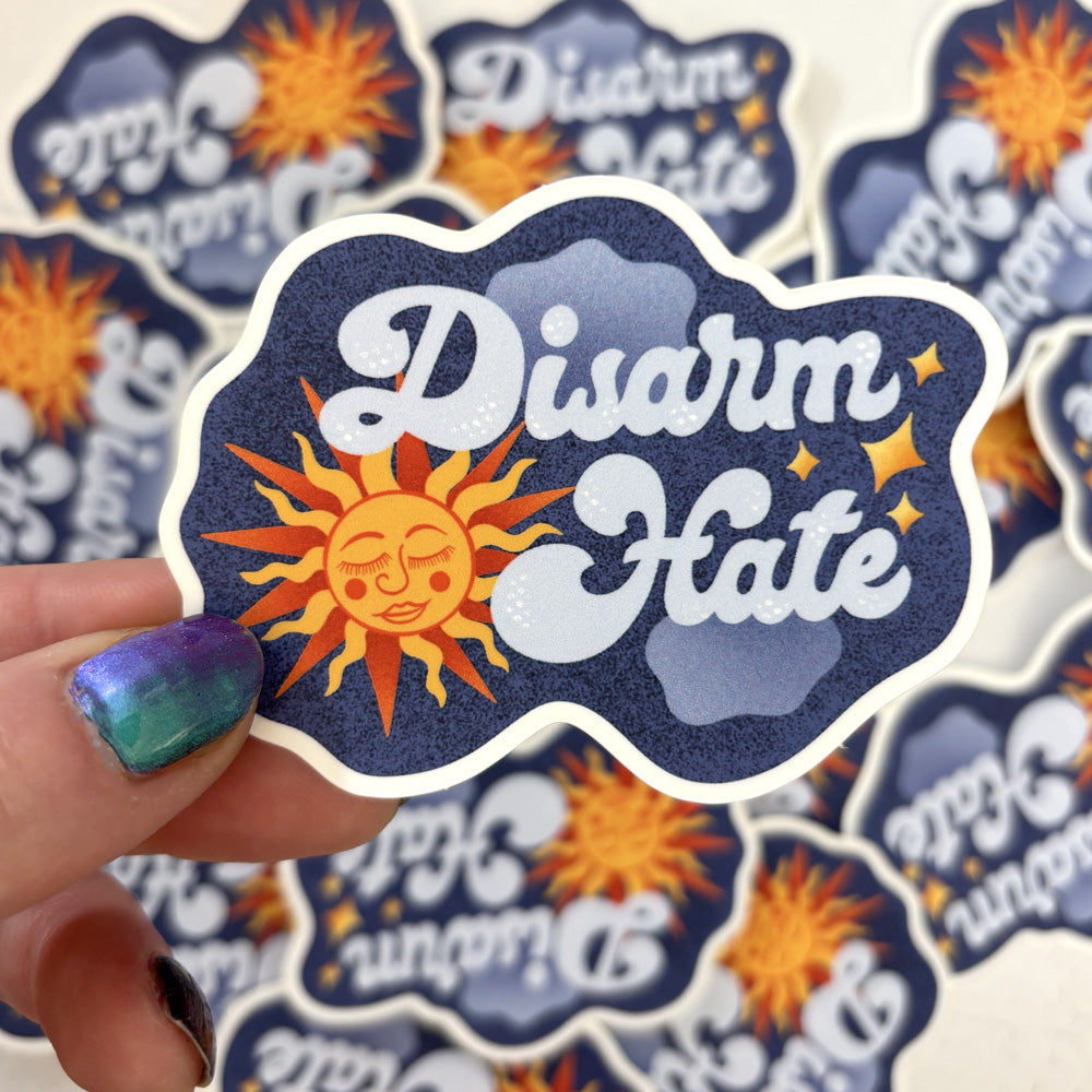 Sticker with 'Disarm Hate' design held by a hand, surrounded by more stickers.