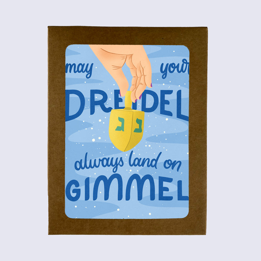 A greeting card with a blue background featuring text and an illustration of a dreidel, with the wish 'May your dreidel always land on gimmel' 