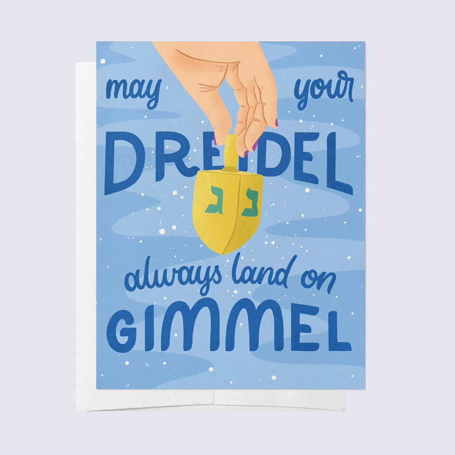 A greeting card with a blue background featuring a graphic of a dreidel and the text 'May your dreidel always land on Gimmel' in a stylized lettering