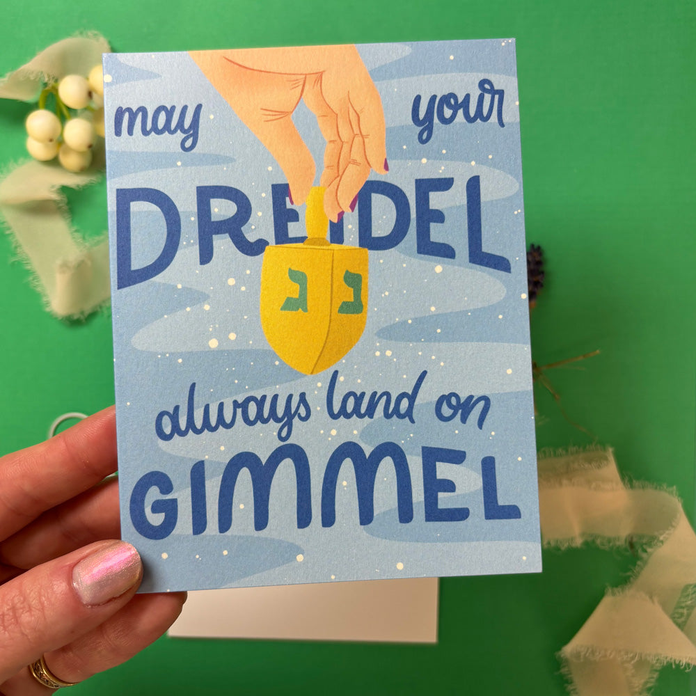 Card with a dreidel illustration and text held by a hand against a green background