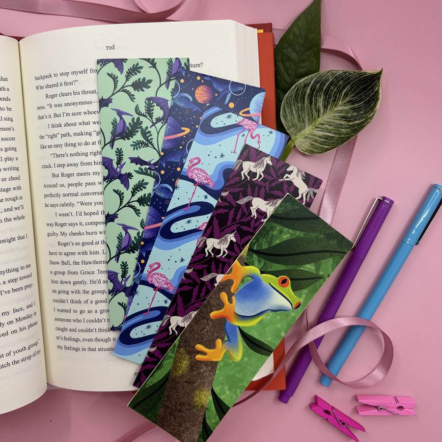 Colorful bookmarks with nature-themed designs on an open book, surrounded by stationery items on a pink background.