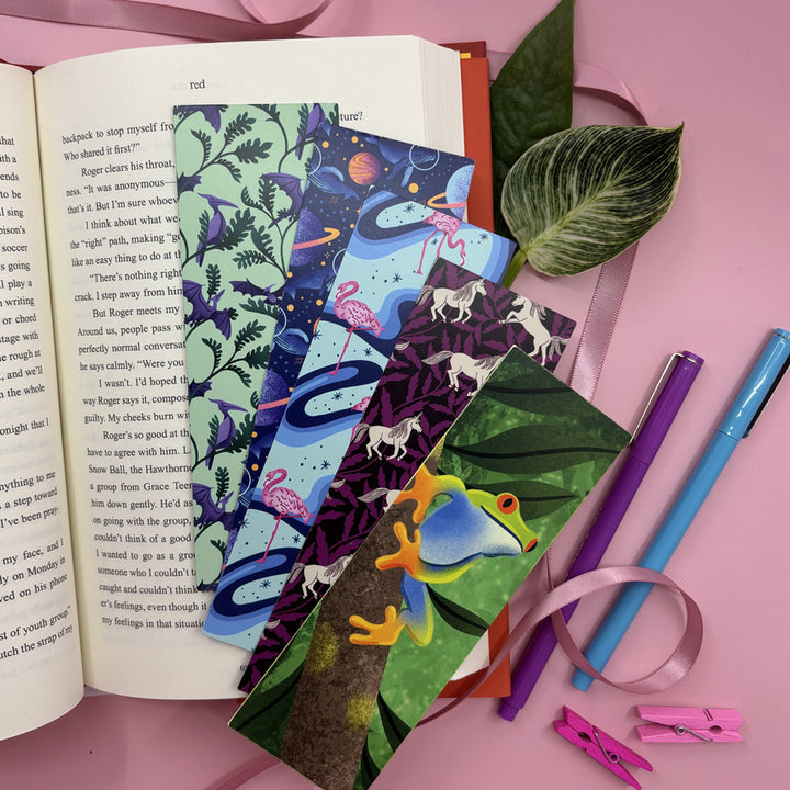 Colorful bookmarks with nature-themed designs on an open book, surrounded by stationery items on a pink background.