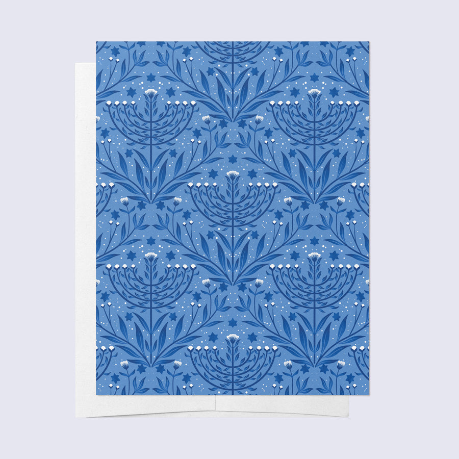 A folded greeting card with a blue background and a white floral Menorah pattern, paired with a bright white envelope.