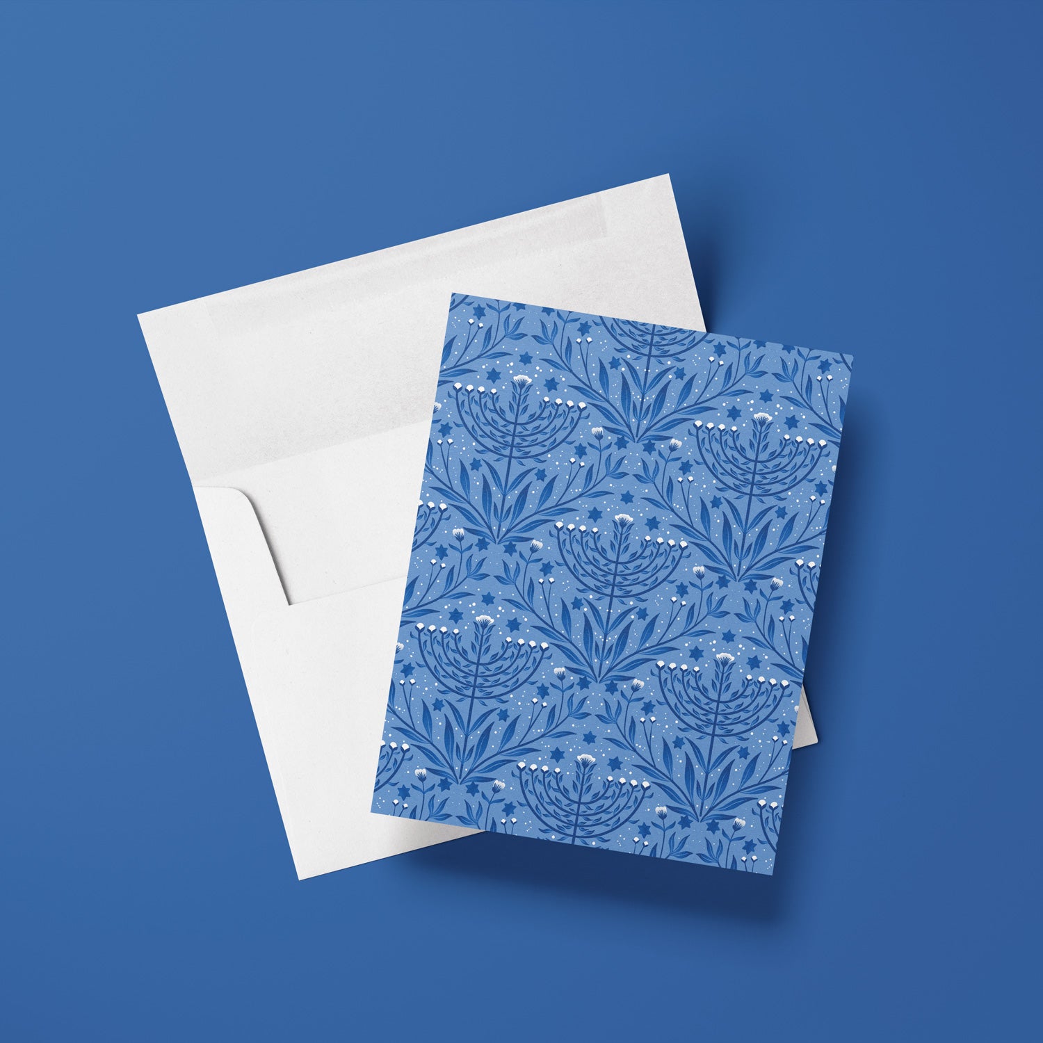 Blue floral menorah patterned card with white envelope on a blue background
