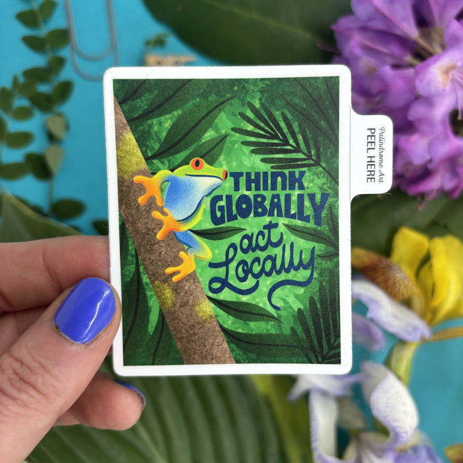 Card with a frog illustration and 'Think Globally, Act Locally' text held by a hand against a floral background.