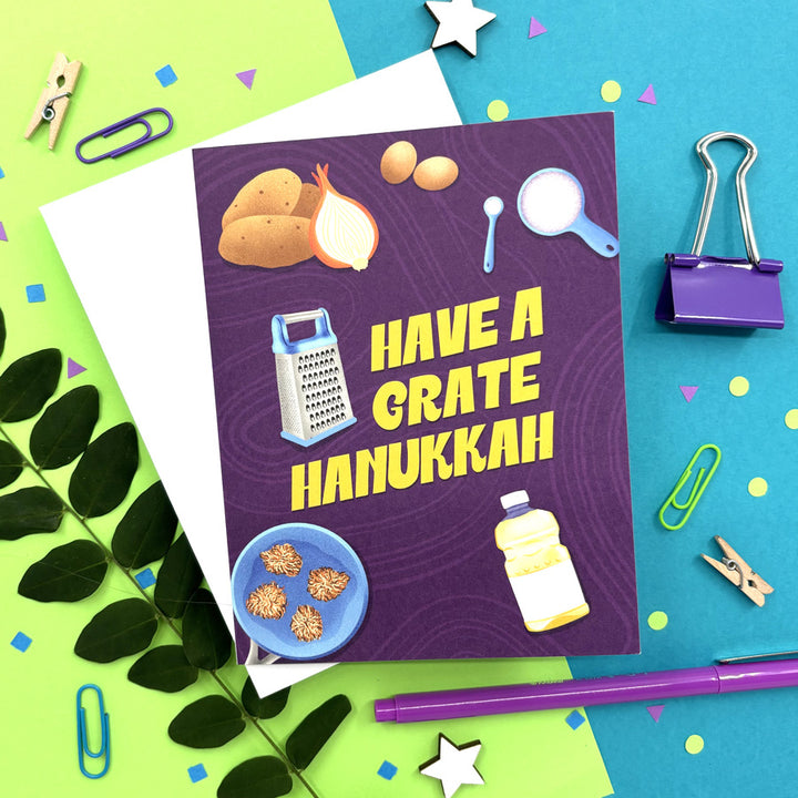 Hanukkah card with illustrated potato latke ingredients and text "have a grate hanukkah" on a bright background
