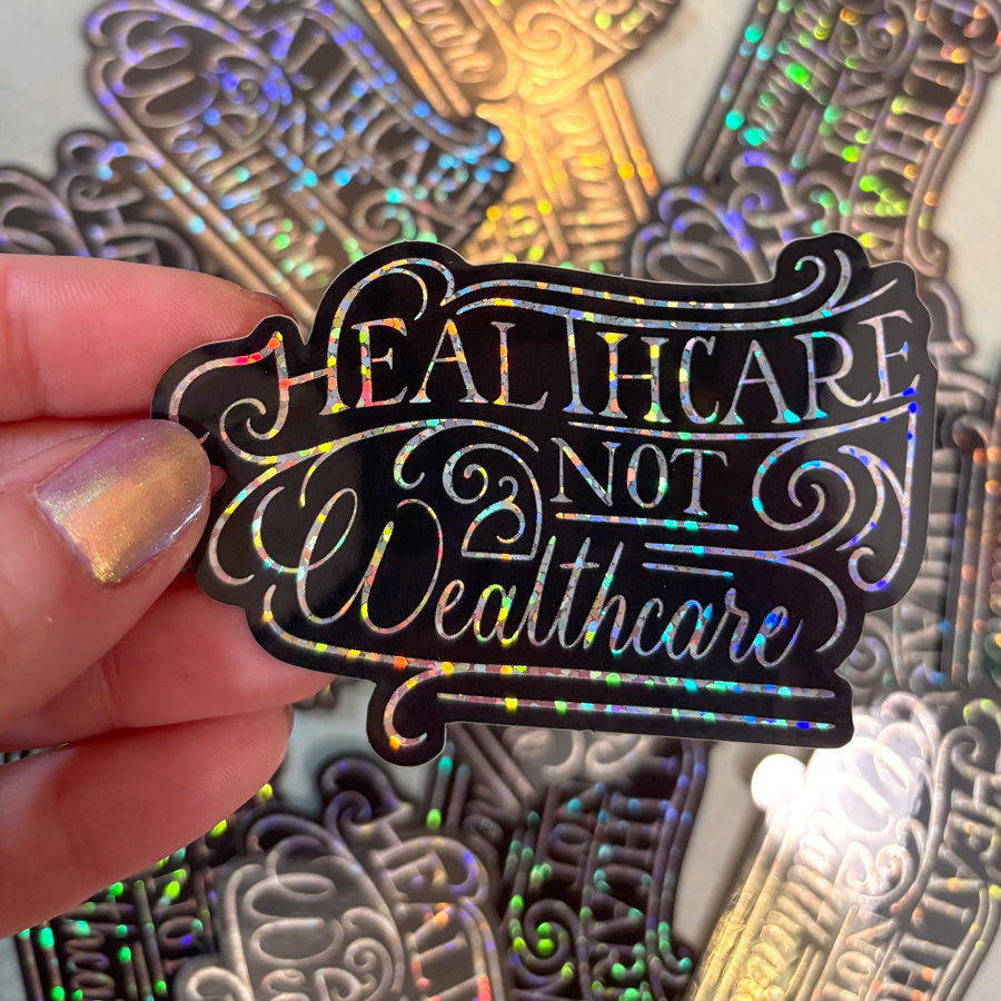 Holographic 'Healthcare Not Wealthcare' sticker held by a hand with colorful nail polish.