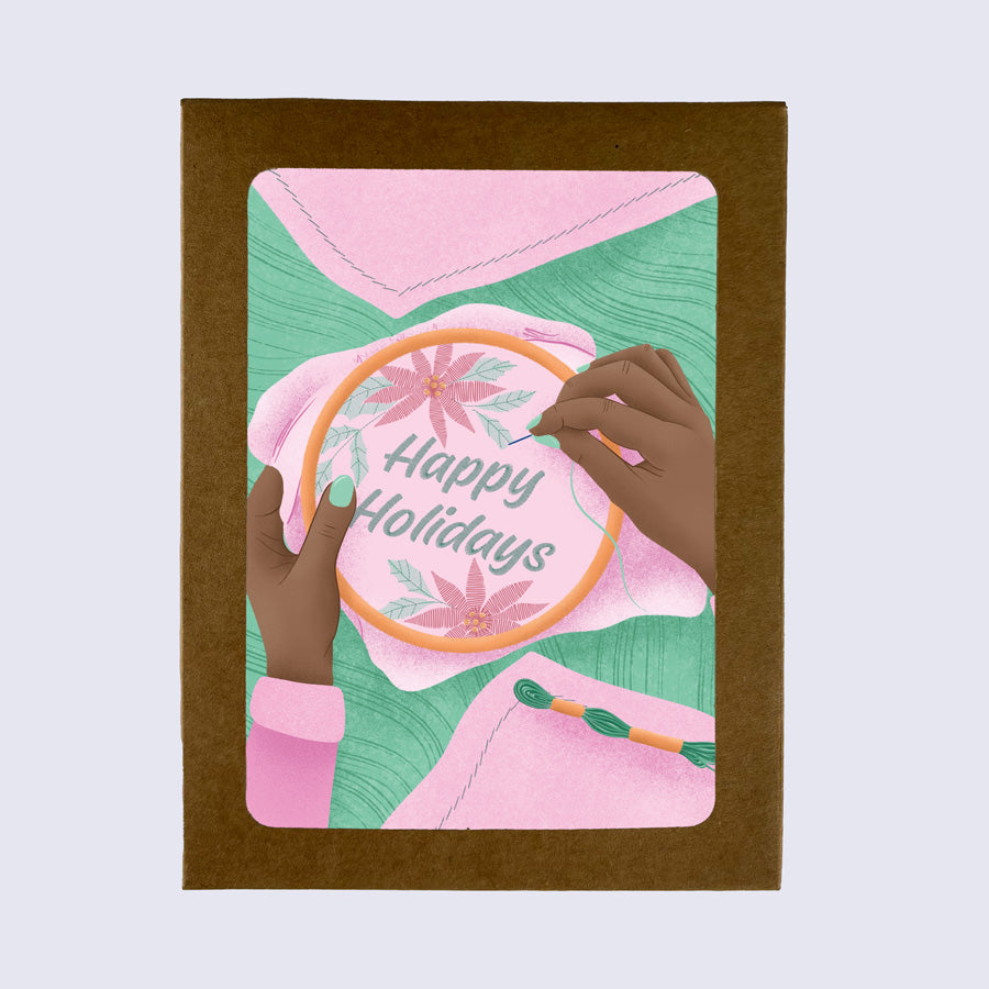 A folded greeting card with 'Happy Holidays' text and an embroidered design featuring flowers and a needle.