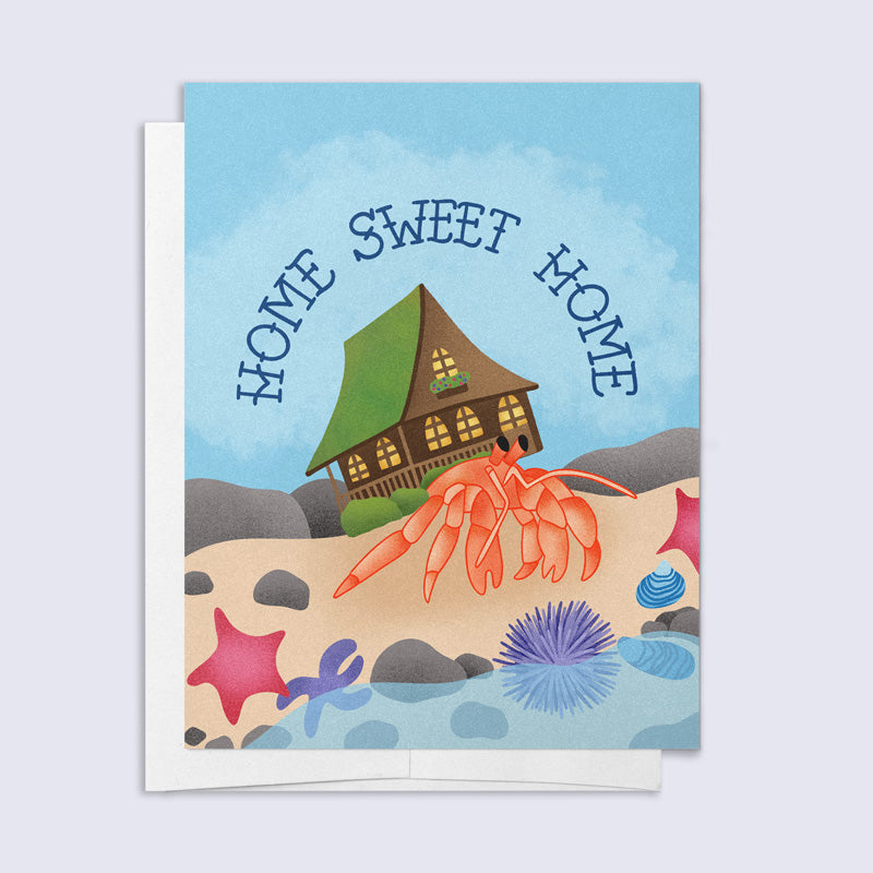 Greeting card with a house, crab, and 'Home Sweet Home' text on a beach scene.