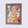 A square kraft paper gift box with a clear window showing a Rosh Hashana greeting card with a honey bear illustration. The bear holds a label that reads L'shana tova and is surrounded by red apples and green leaves on a light blue background.