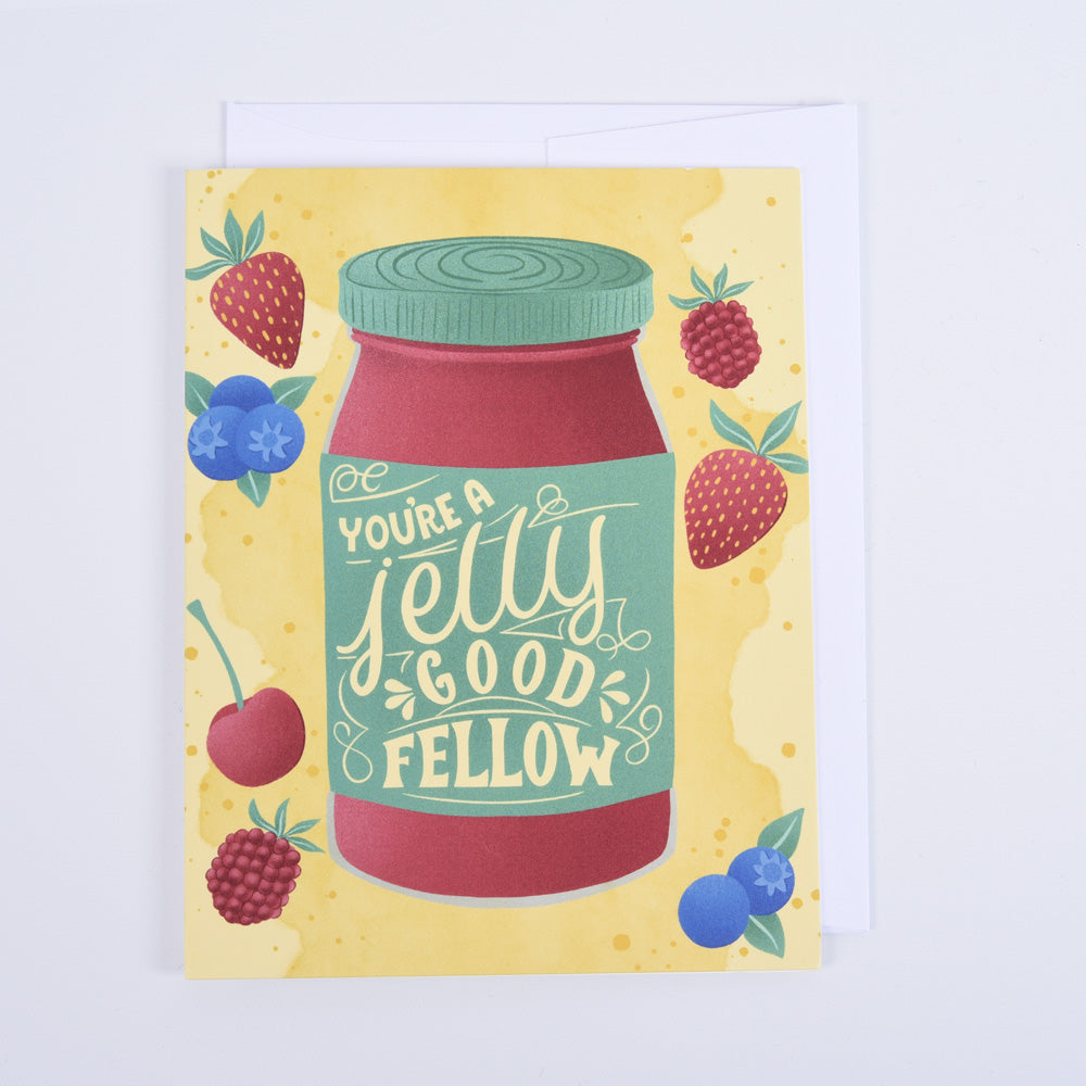 A folded greeting card with a colorful design featuring a strawberry jelly jar and the text 'You're a Jelly Good Fellow,' surrounded by berries on a yellow background.