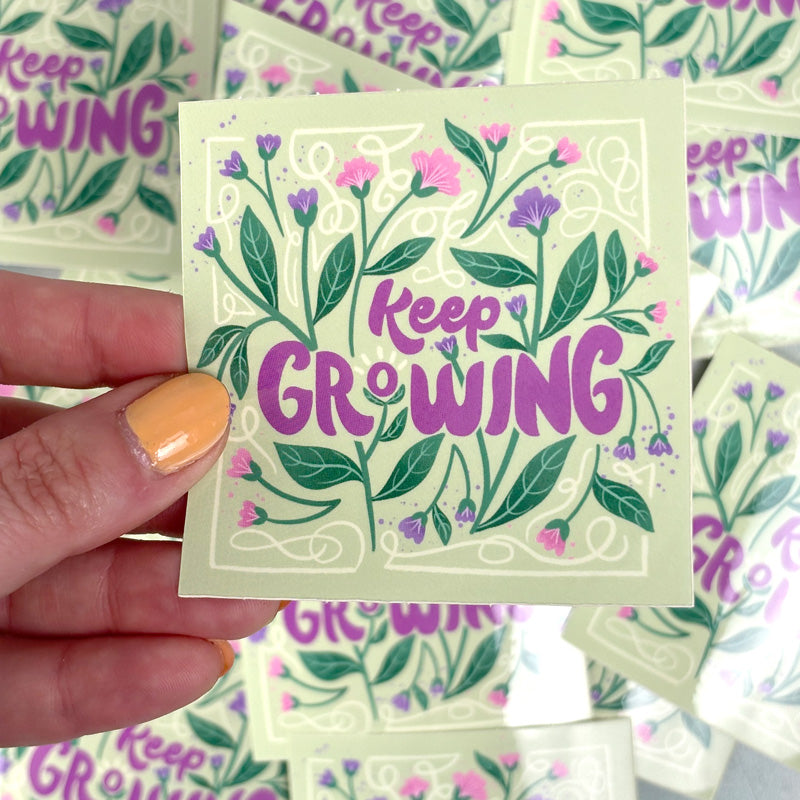 hand holding A sticker with a floral design and the text 'Keep Growing' in purple.