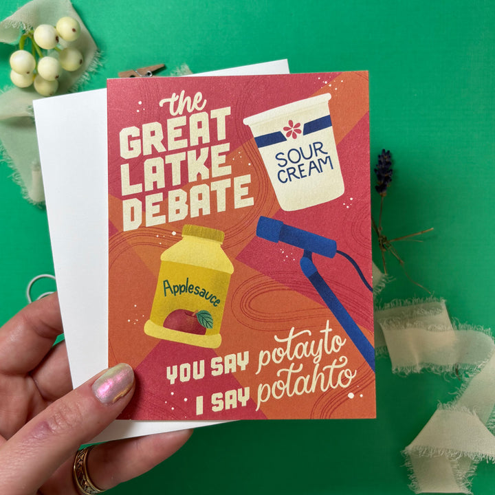 Card with 'The Great Latke Debate' design featuring sour cream, applesauce, and a potato masher on a green background.
