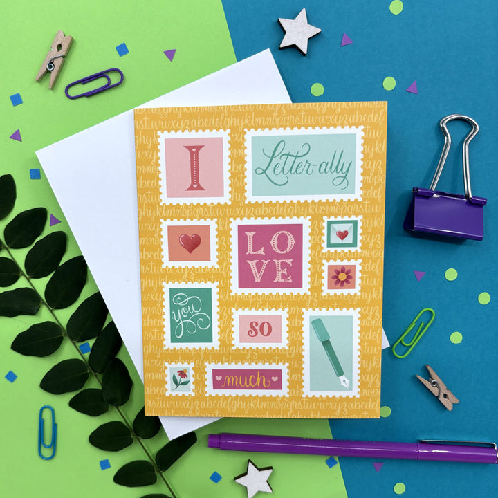 greeting card with illustrated stamps that says "I letter-ally love you so much" on a colorful background ith stationery items