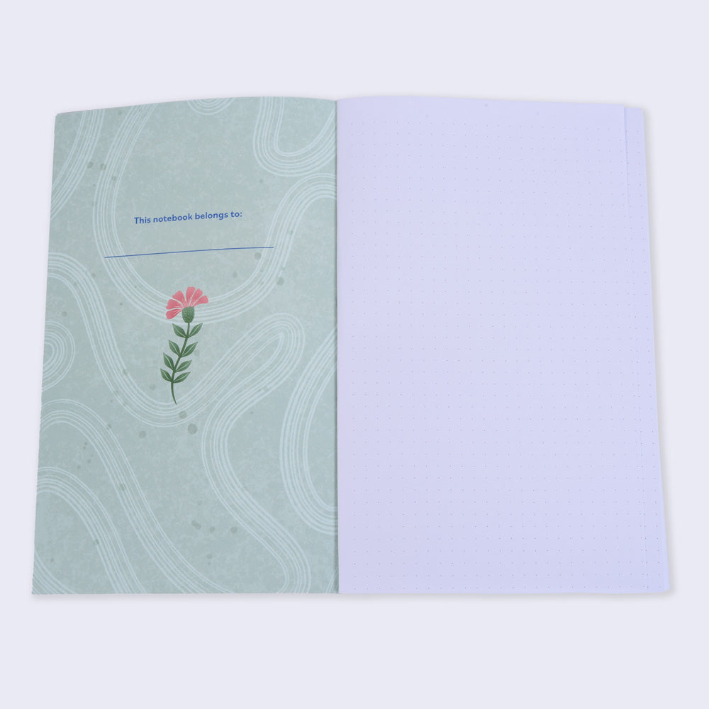 open flat lay notebook with dot grid pages, left inside cover is green and has a small illustrated flower and text "this notebook belongs to"