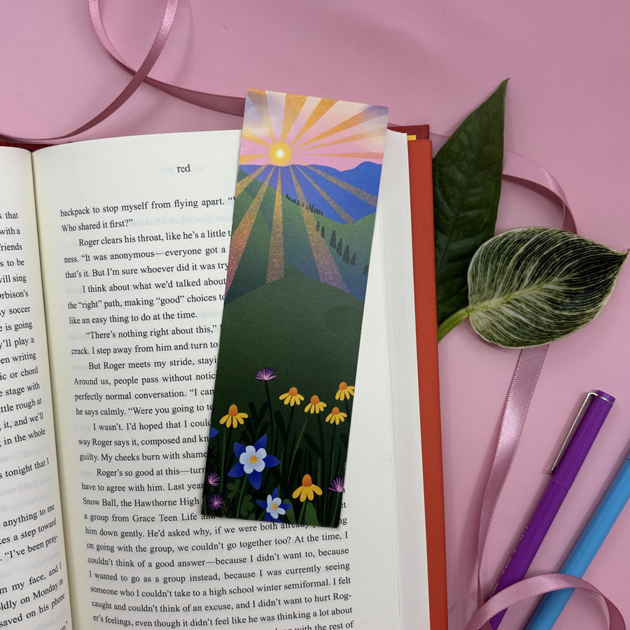 Colorful bookmark with a nature design on an open book against a pink background