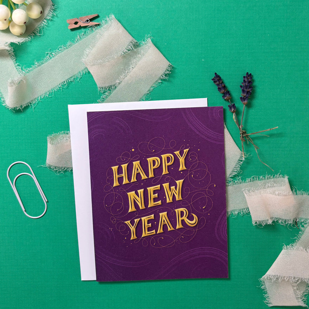 Purple 'Happy New Year' card on a green background with decorative elements.