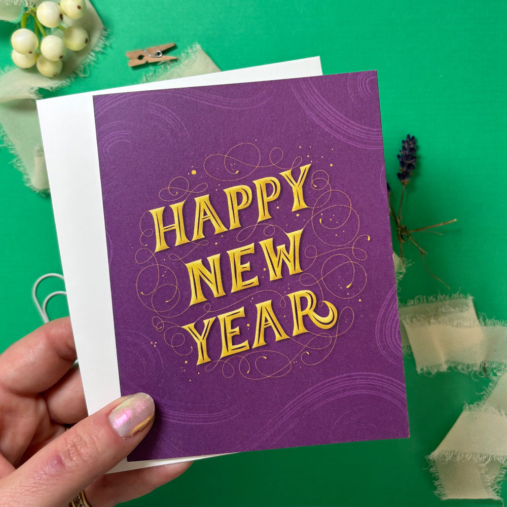 Purple 'Happy New Year' card held by a hand on a green background