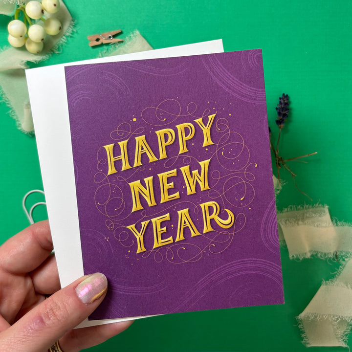 Purple 'Happy New Year' card held by a hand on a green background